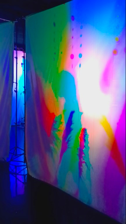 A dancer moves gracefully in the 'Magical Colored Shadows Playground' art installation, casting vibrant and ever-changing colored shadows.