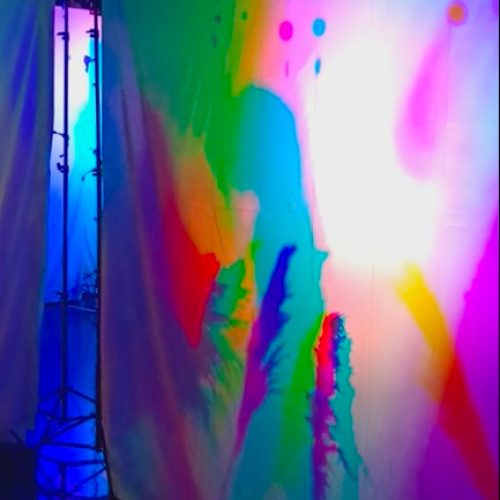 A dancer moves gracefully in the 'Magical Colored Shadows Playground' art installation, casting vibrant and ever-changing colored shadows.